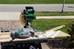 a circular saw sits on top of some wood in front of a sidewalk and grass