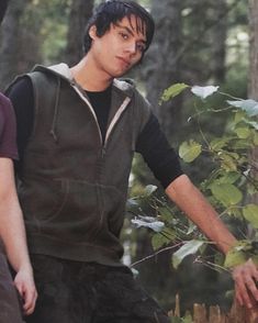 two young men standing next to each other in the woods