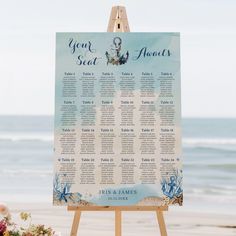 an easel with a seating chart on it next to flowers near the ocean shore