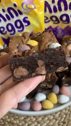 a hand holding a piece of brownie next to some candy