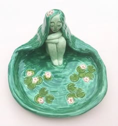 a ceramic figurine sitting on top of a bowl filled with water lilies