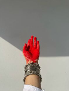 a woman's hand with red paint on it and bracelets around her wrist