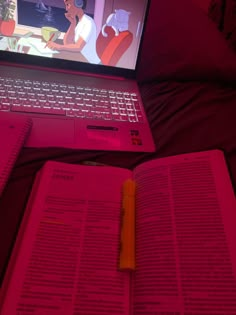 an open laptop computer sitting on top of a bed next to a book and pen