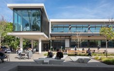 people are sitting at tables in front of a building with glass walls and large windows