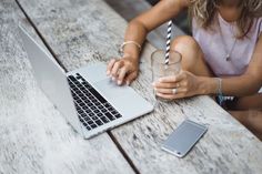 a woman sitting at a wooden table with a laptop and drink in front of her