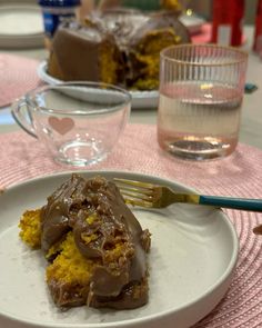 a piece of cake with chocolate frosting on a plate next to a glass of water