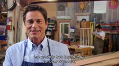 a man with an apron on standing in front of a table and talking to someone