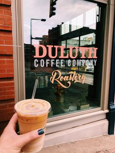 a hand holding a cup of coffee in front of a window