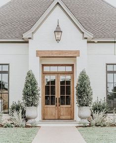 a white house with two wooden doors and three planters on the front lawn in front of it