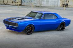 a blue muscle car parked in front of a wall with graffiti on it's side