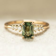 a ring with an emerald colored stone surrounded by three white diamonds on top of it