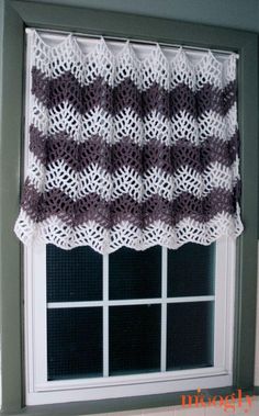 a crocheted window valance hanging on the side of a wall in front of a window