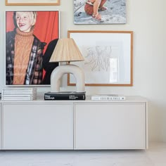 a white sideboard with pictures on the wall above it and a lamp next to it