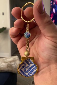 a hand holding a blue and white keychain that has a small round object hanging from it