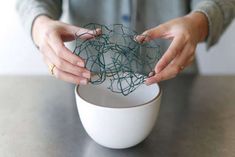 a woman holding something in her hands over a white bowl on a counter top,