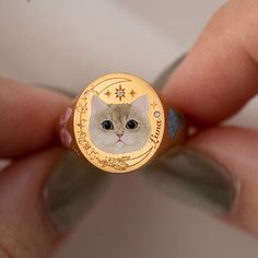 a person holding a gold ring with a cat on it's face in the middle