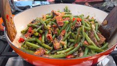 a red pan filled with green beans and bacon