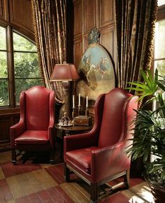 two red leather chairs sitting in front of a window next to a table with lamps on it