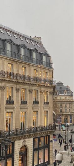 people walking on the sidewalk in front of a building with many windows and balconies