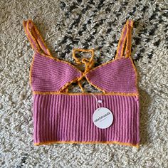 a pink and orange knitted top with a tag attached to the front, laying on a carpet