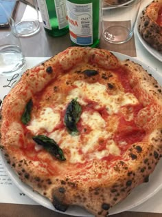 two pizzas sitting on top of a white plate next to bottles of water and glasses