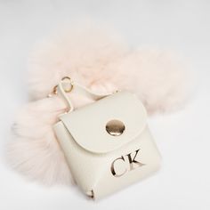 a white purse with a fur ball hanging from it's side on a white surface