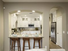 a kitchen with two bar stools in front of the counter and an archway leading to the living room