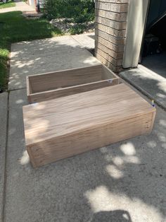 two wooden boxes sitting on the sidewalk next to a brick building with grass and trees in the background