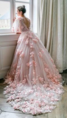 a woman in a pink wedding dress standing by a window with flowers all over it