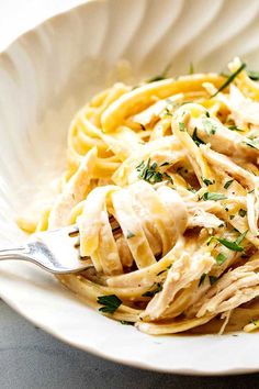 a white bowl filled with pasta covered in chicken and parsley on top of a table