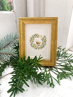 a frame with a wreath on it sitting next to some pine needles and evergreen branches