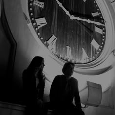 two women sitting in front of a large clock