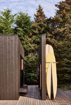 two surfboards are propped up against the side of a wooden building with trees in the background