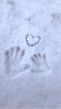 a person's hand and foot prints in the snow with a heart on it