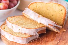 sliced bread with icing sitting on top of a cutting board next to a bowl of fruit