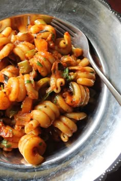 a silver bowl filled with pasta and sauce on top of a table next to a fork