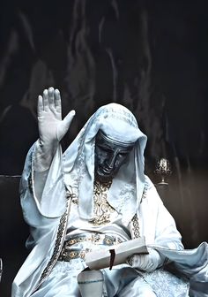 the statue is dressed in white and holds his hand up to catch something while sitting down