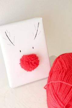 a red ball of yarn next to a white box with a face drawn on it