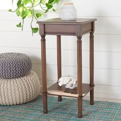 a small wooden end table on a rug next to a potted plant and pillow