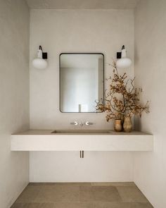 a bathroom with a sink, mirror and vases on the counter in front of it