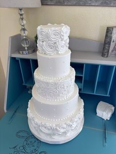 a large white wedding cake sitting on top of a blue table next to a lamp