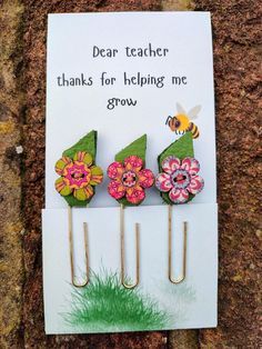 three flowers and a bee are on top of some paper clips with the words dear teacher thanks for helping me grow