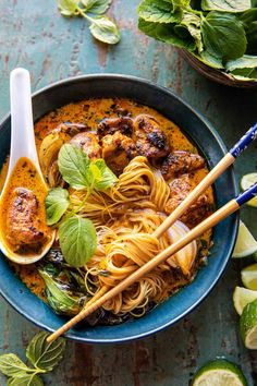 a bowl filled with noodles, meat and vegetables on top of a blue table next to sliced limes