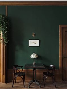 two chairs and a table in a room with dark green paint on the walls, along with a potted plant