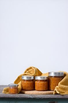 four jars of jam sitting on top of a wooden table next to a yellow towel