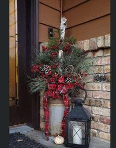 a christmas decoration with pine cones and berries in a pot next to a lantern on the front porch