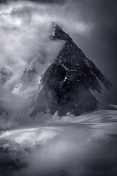 a mountain covered in snow and clouds under a cloudy sky with dark clouds over it