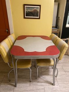 a dining room table with four chairs and a painting hanging on the wall above it