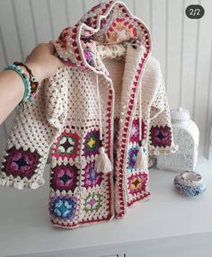 a crocheted jacket is being held up by someone's hand on a table