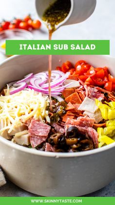 the ingredients for italian sub salad are being poured in a large bowl with a spoon